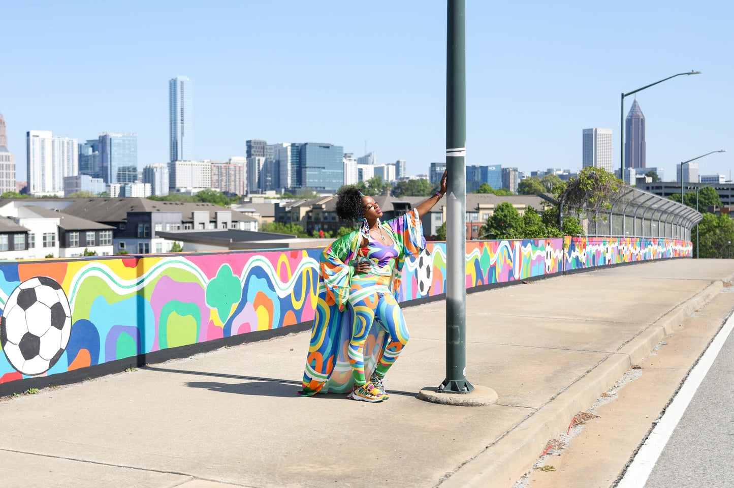 Melissa Mitchell standing beside her FIFA 2026 mural on the 17th Street Bridge in Atlanta, a colorful public art installation commissioned by the City of Atlanta near Atlantic Station.